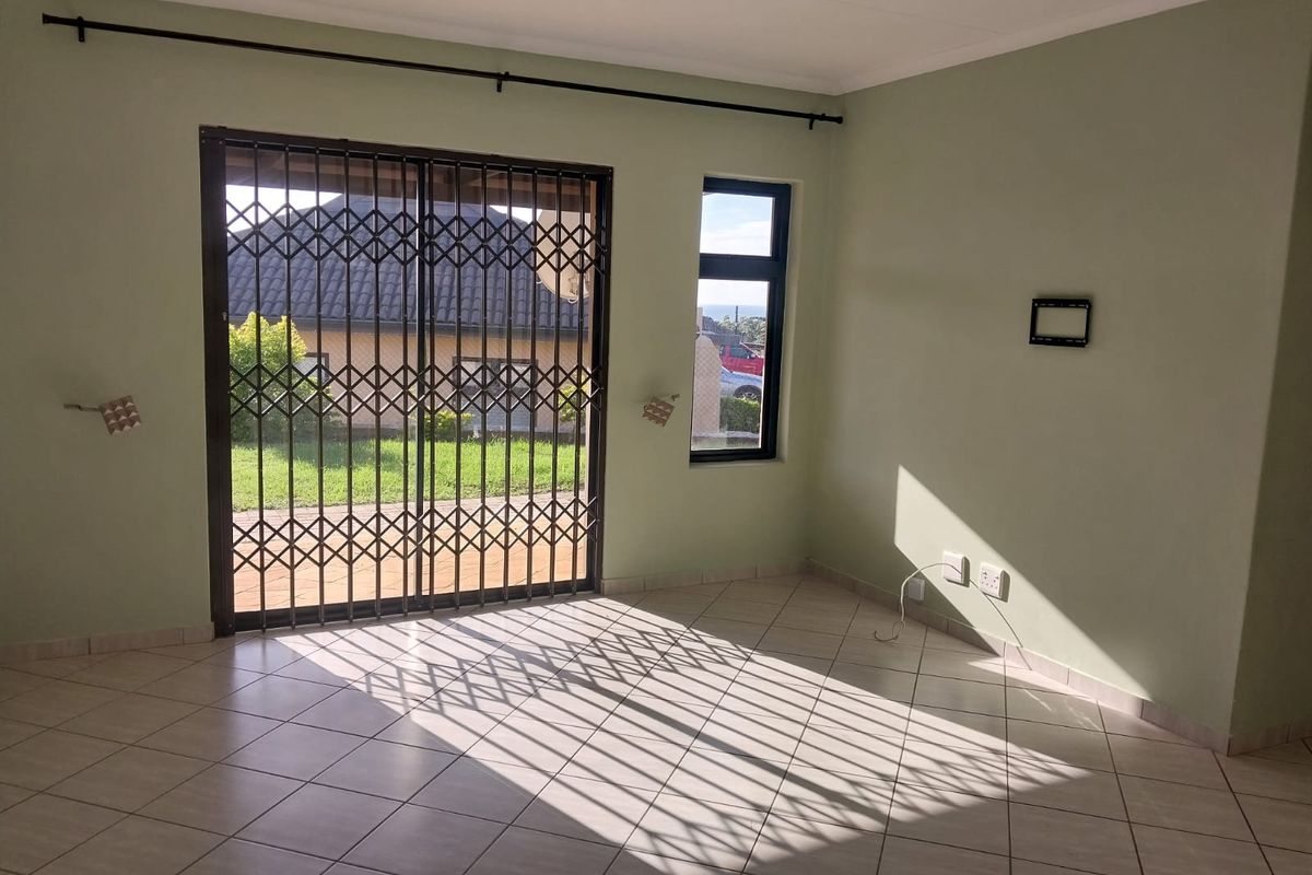 An empty living room featuring tiled flooring, a sliding glass door with a security gate, and natural light through a side window.