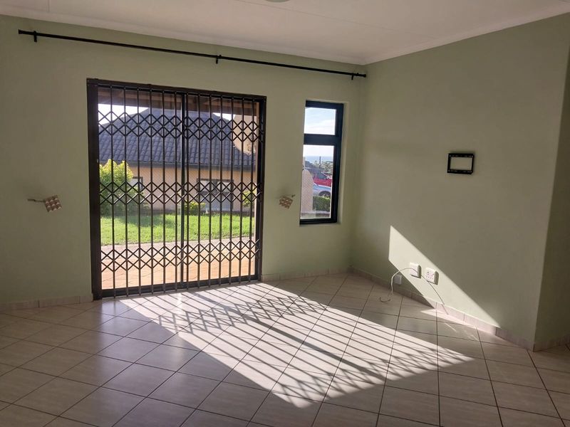 An empty living room featuring tiled flooring, a sliding glass door with a security gate, and natural light through a side window.