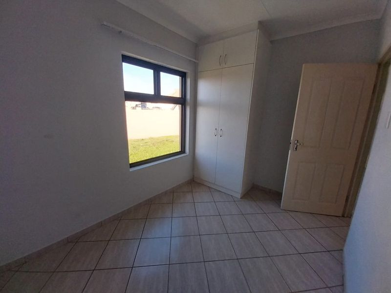 A clean, empty bedroom featuring neutral tiled flooring, built-in cupboards, and a window providing natural light.