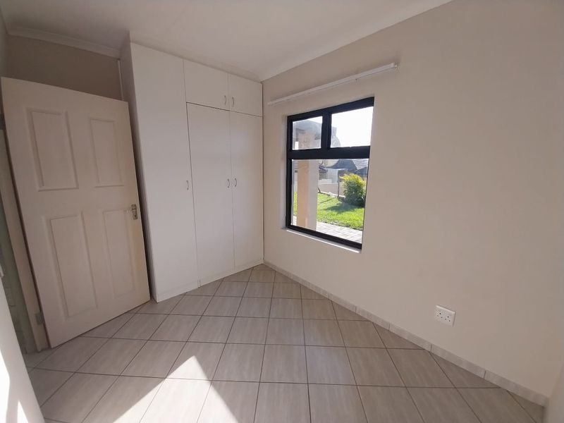 A bright, empty bedroom featuring neutral tiled flooring, built-in cupboards, and a large window providing natural light.