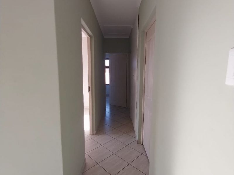 A clean, neutral-toned hallway featuring diagonal tiled flooring and access to multiple rooms.