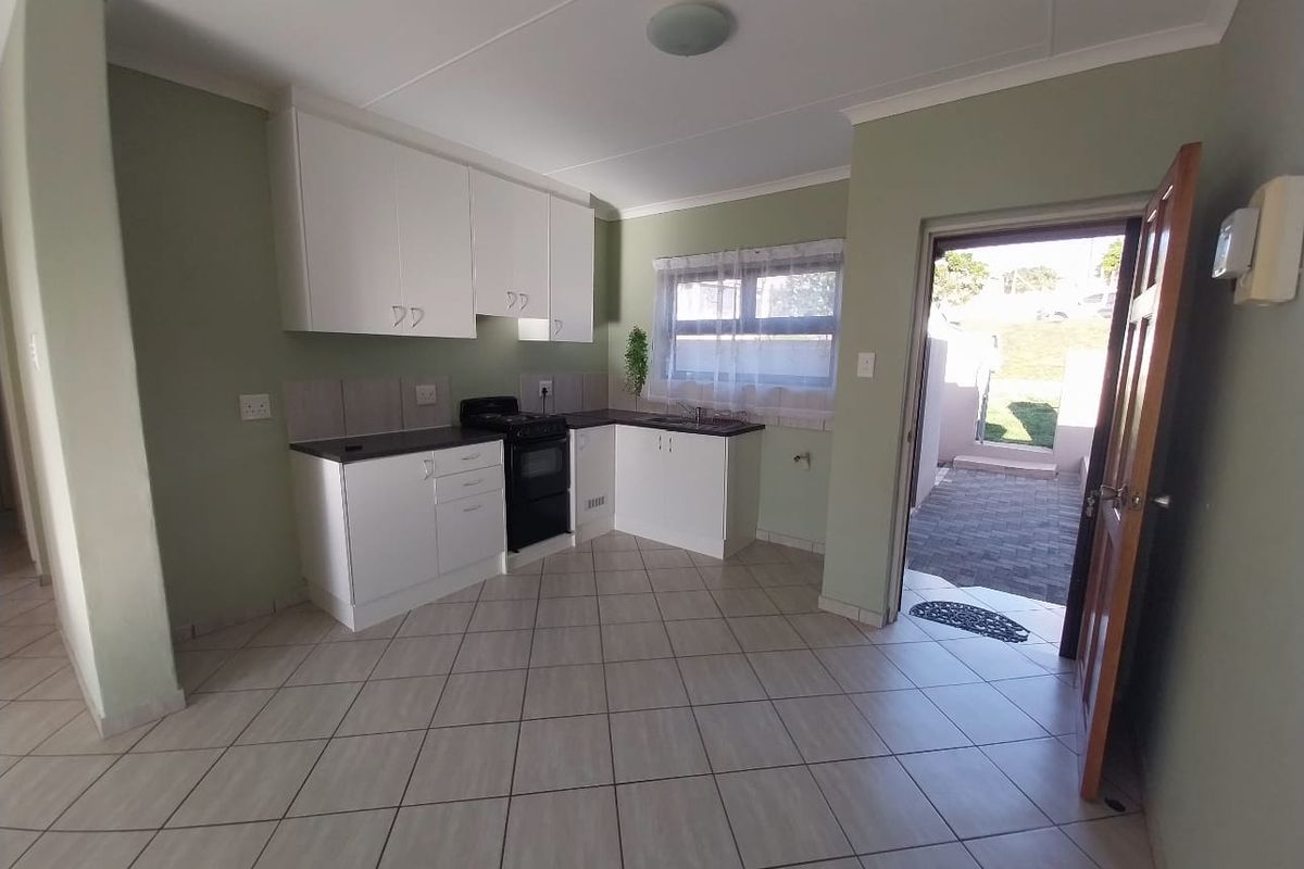 A functional kitchen featuring white cabinetry, dark countertops, tiled flooring, and a freestanding stove, with direct access to an outdoor paved area.