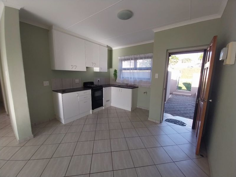A functional kitchen featuring white cabinetry, dark countertops, tiled flooring, and a freestanding stove, with direct access to an outdoor paved area.