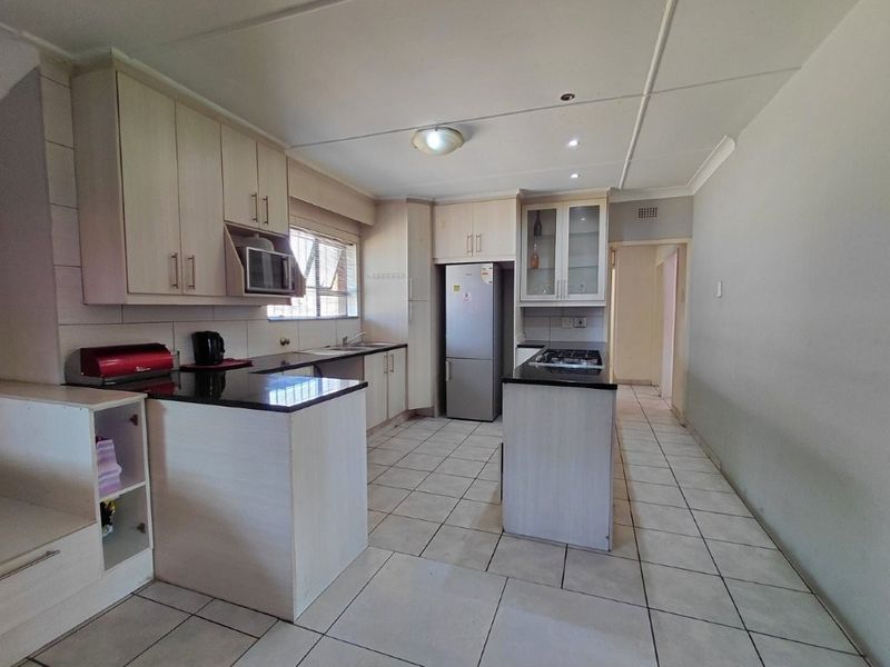 A functional kitchen featuring light-toned built-in cabinetry, granite countertops, a gas hob, and tiled flooring, offering a clean and practical workspace.