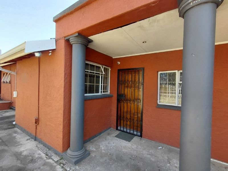 Front entrance area featuring a covered porch with decorative columns, a timber door with security gate, and aluminium window frames.