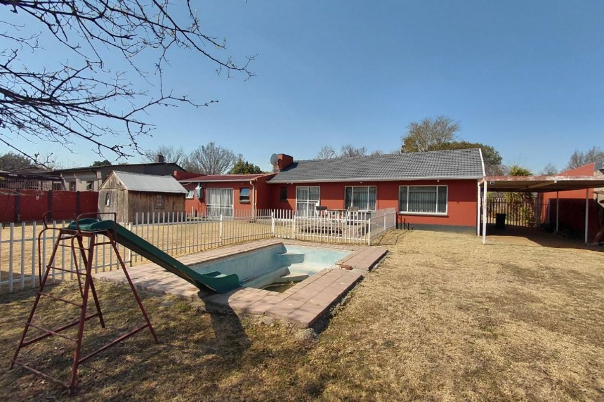 Rear view of the property featuring a swimming pool, fenced garden area, carport, and direct access to the home via sliding doors.