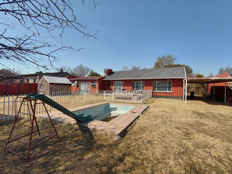 Rear view of the property featuring a swimming pool, fenced garden area, carport, and direct access to the home via sliding doors.