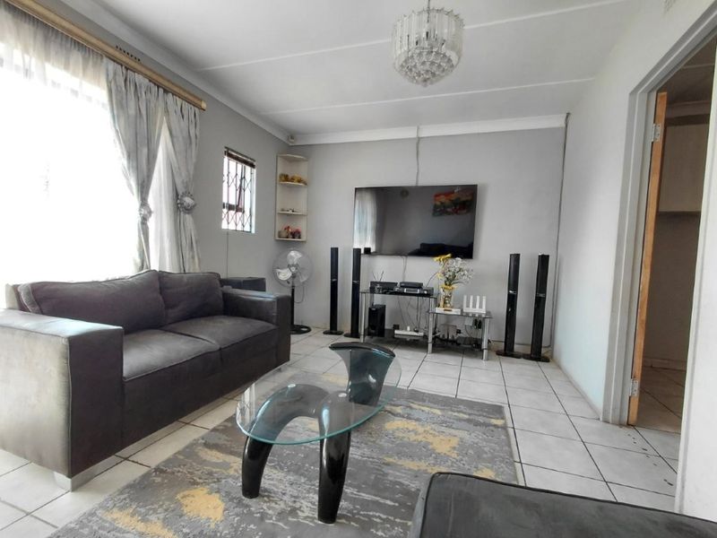 A living room featuring tiled flooring, built-in corner shelving, and a window with security bars, providing a functional and well-lit living space.