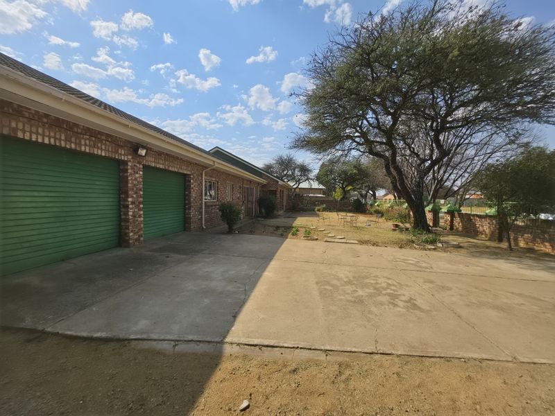 Rear exterior view featuring a double garage with green roller doors, a concrete driveway, and a spacious garden area with mature trees.