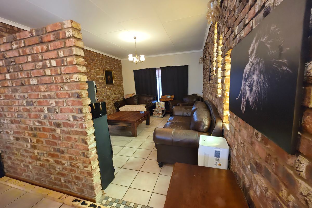 Living room featuring exposed brick walls, tiled flooring, and integrated wall lighting, offering a rustic aesthetic with potential for modern updates.