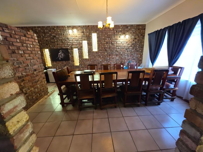 A spacious dining room featuring a prominent exposed brick feature wall, ceramic tiled flooring, and integrated wall lighting.