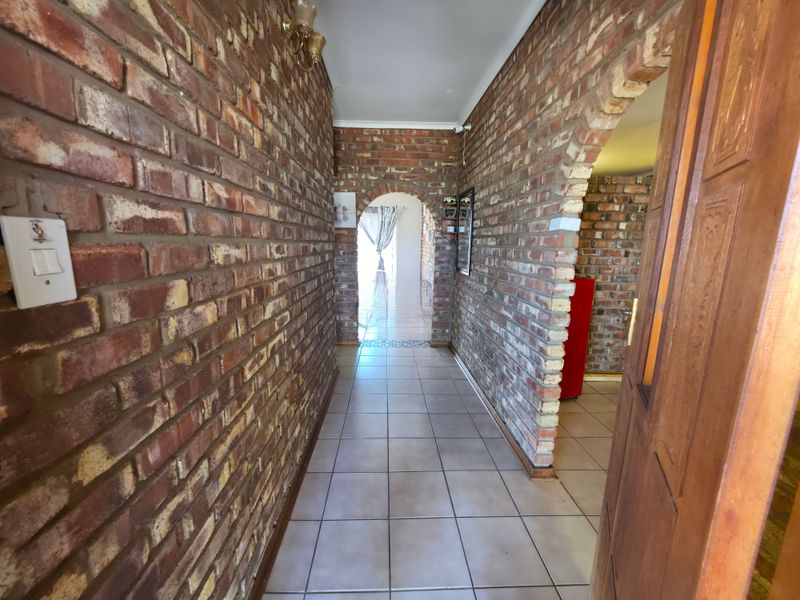 A spacious hallway featuring rustic exposed brick walls, ceramic floor tiles, and a distinctive arched entryway leading to adjacent living areas.