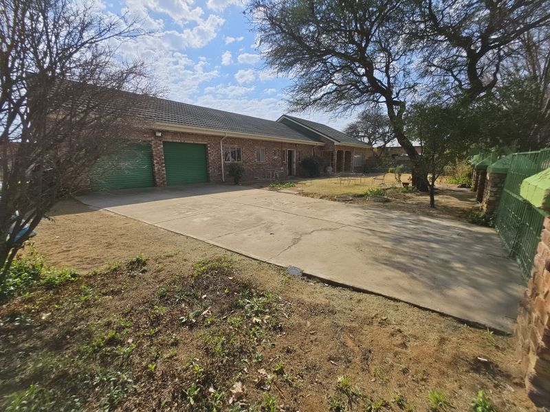 Front view of a single-story brick house featuring a double garage, concrete driveway, and established garden area.