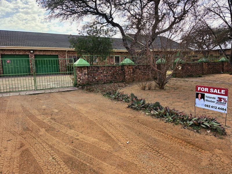 Front exterior view of a single-story brick house featuring a tiled roof, double garage, and secure gated entrance with a paved driveway.