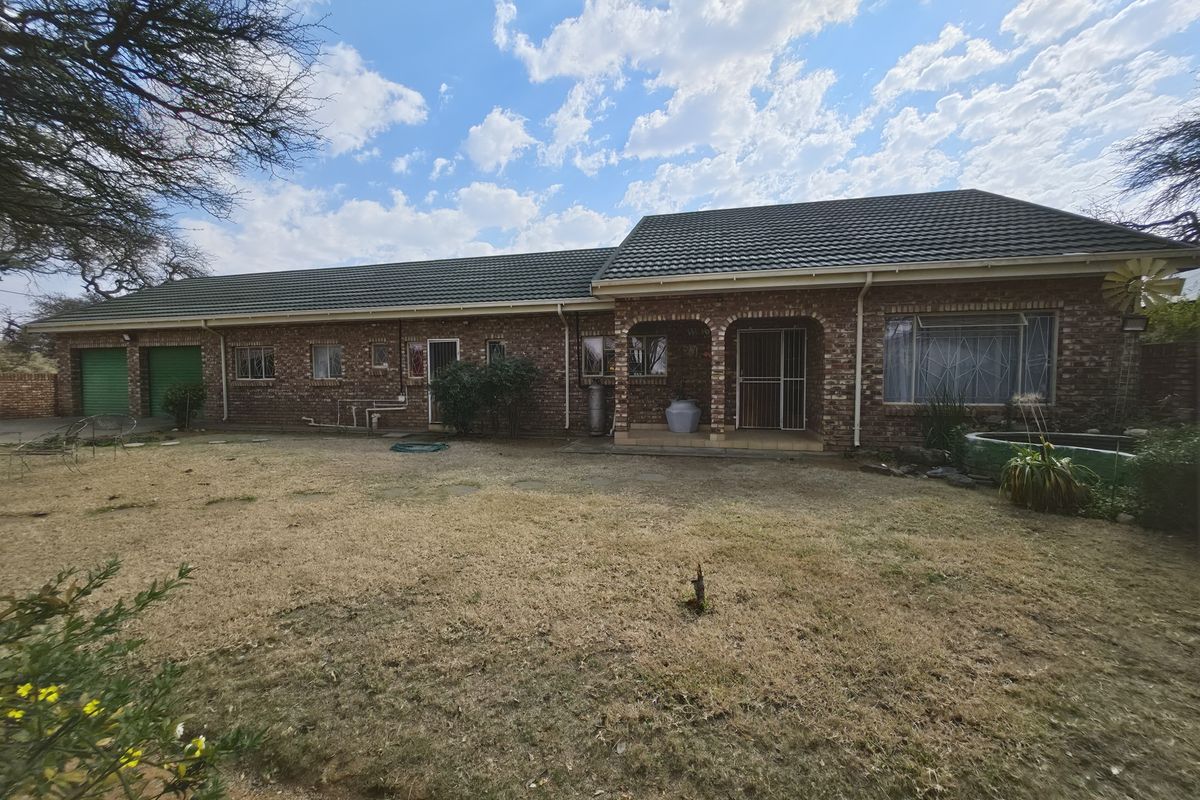 A rear view of a single-story face brick house featuring a tiled roof, integrated garage, and a covered patio area overlooking the garden.