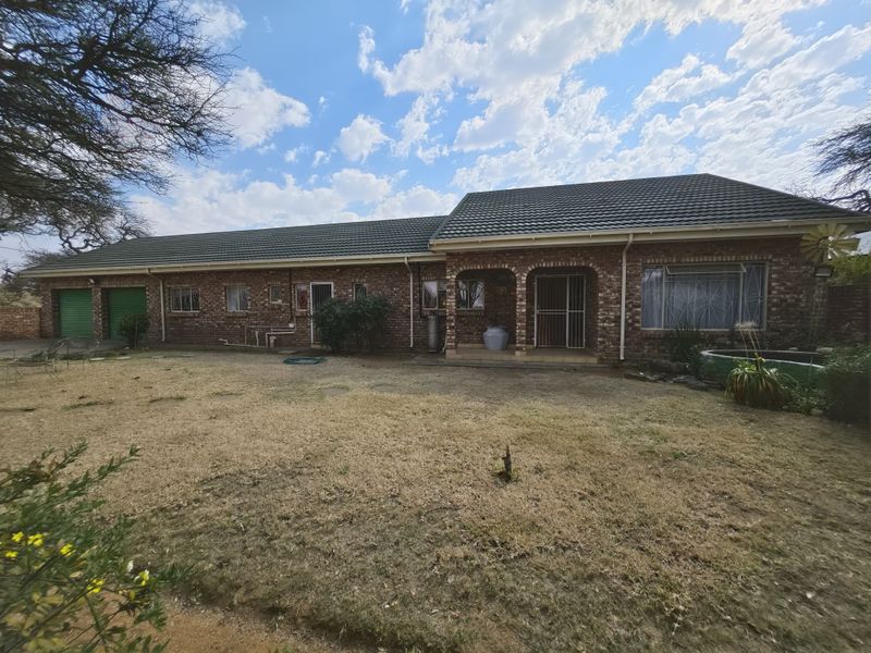A rear view of a single-story face brick house featuring a tiled roof, integrated garage, and a covered patio area overlooking the garden.
