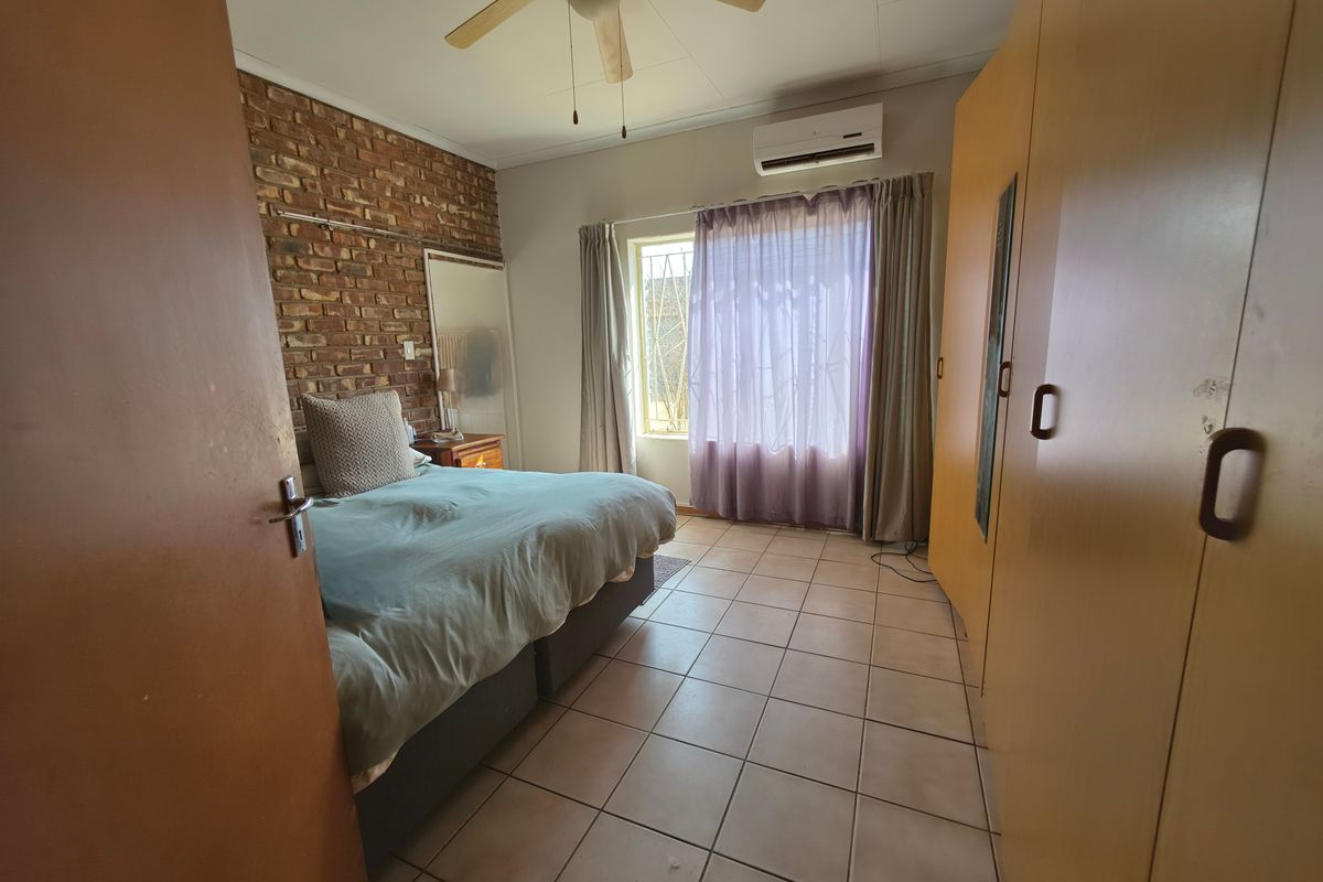 Bedroom featuring tiled flooring, an exposed brick feature wall, built-in cupboards, a ceiling fan, and a wall-mounted air conditioning unit.