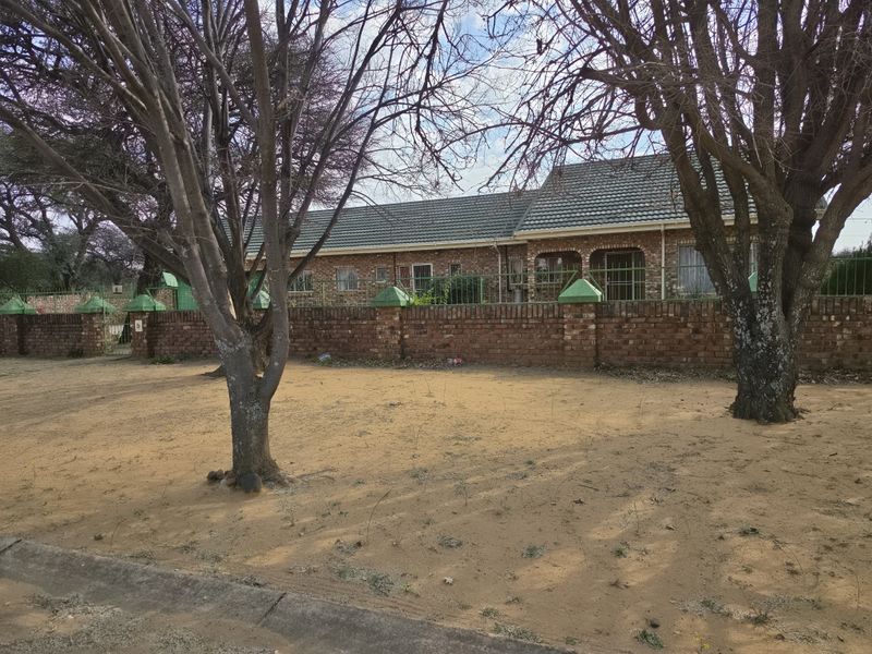 Front view of a single-story face brick house featuring a tiled roof, enclosed by a brick boundary wall and security fencing.