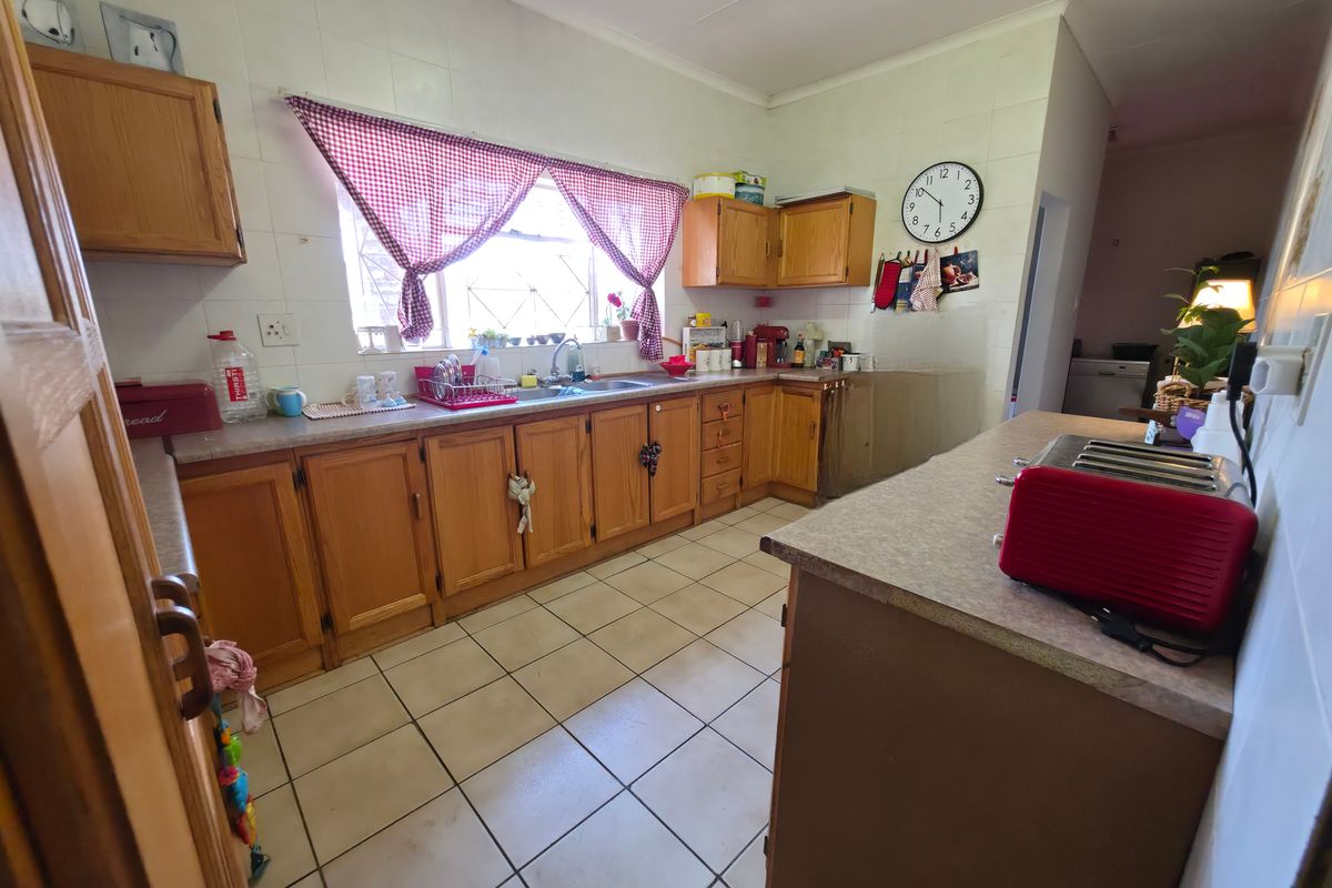 A functional kitchen featuring wooden cabinetry, laminate countertops, a stainless steel sink, and tiled flooring, offering a classic layout with potential for modernization.