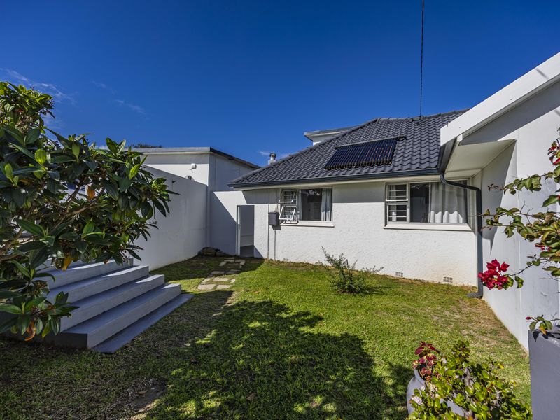 Rear exterior view of the property featuring a well-maintained garden, concrete steps, and a solar water heating system installed on the tiled roof.