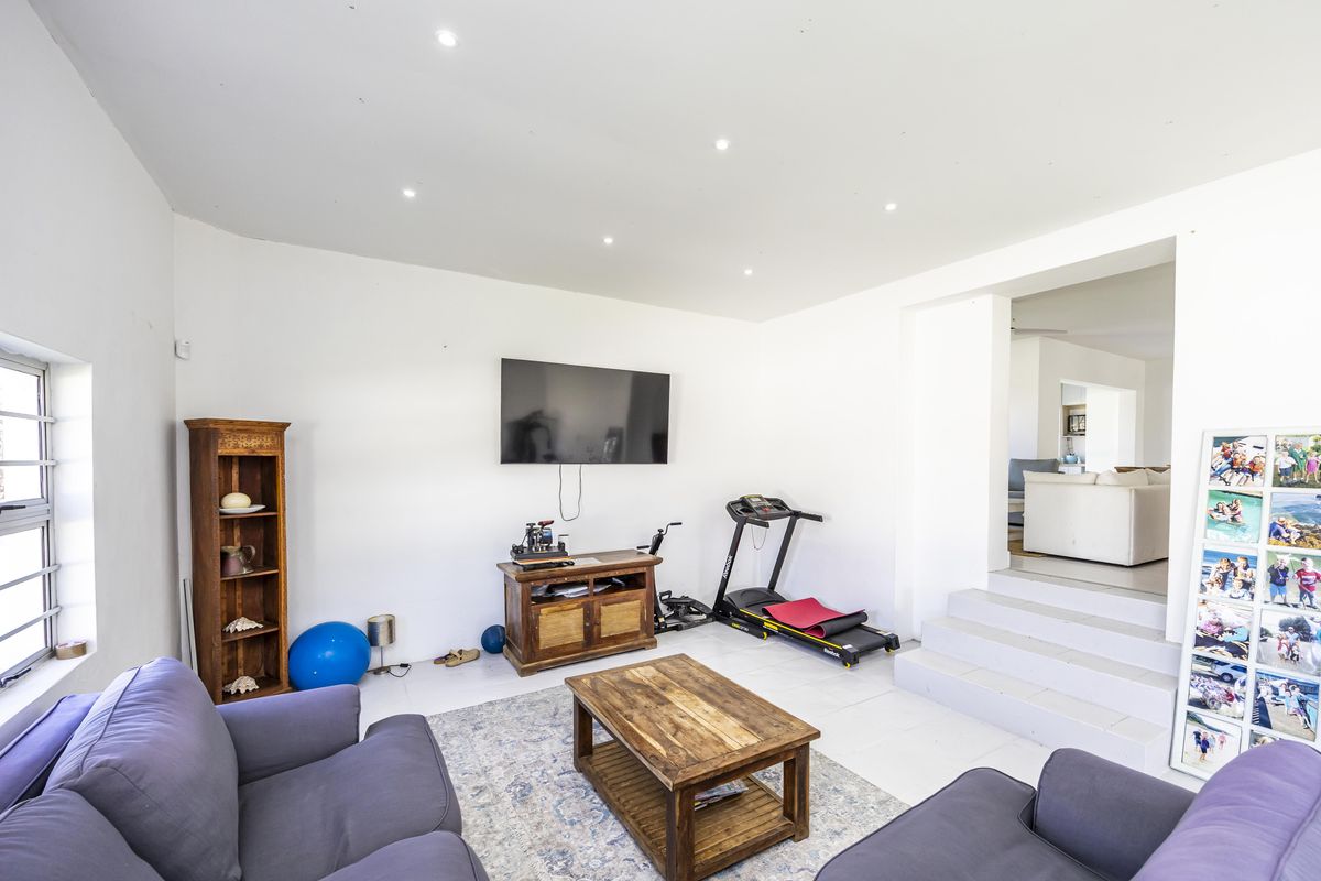 A bright living room featuring tiled flooring, recessed downlights, and a stepped transition leading to an adjacent living space.