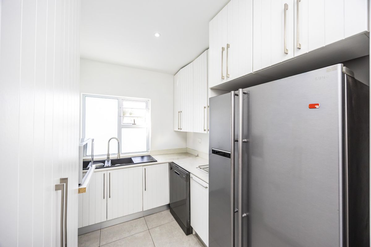 A clean and functional kitchen featuring white cabinetry, tiled flooring, a double sink, and integrated appliances.