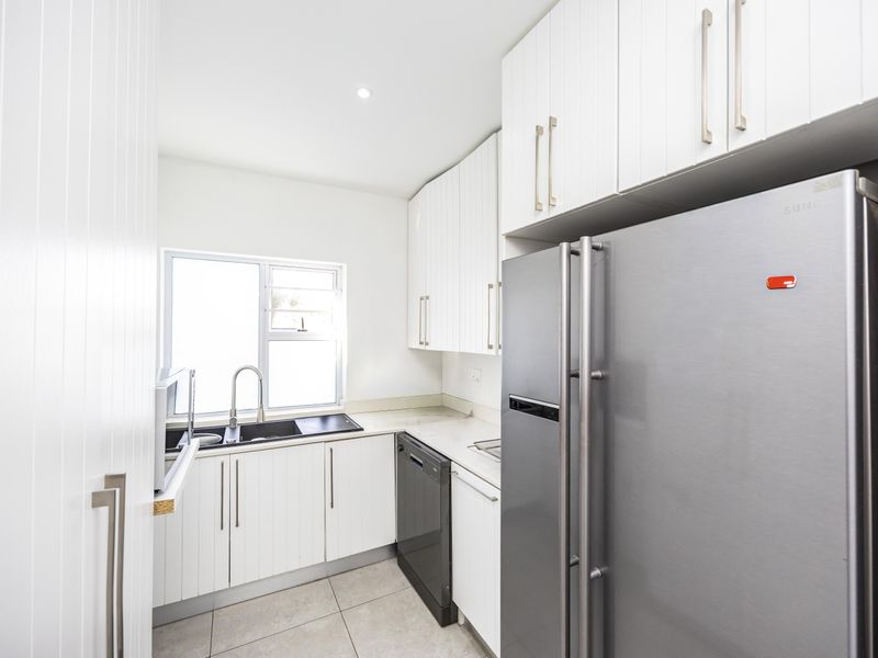 A clean and functional kitchen featuring white cabinetry, tiled flooring, a double sink, and integrated appliances.