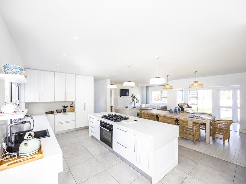 Spacious open-plan kitchen and dining area featuring a large central island, modern white cabinetry, stone countertops, and integrated appliances with abundant natural light.