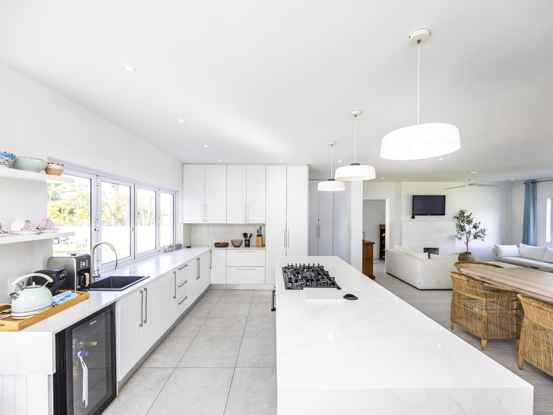 Spacious open-plan kitchen and living area featuring a large central island with gas cooktop, modern white cabinetry, and sleek tiled flooring.