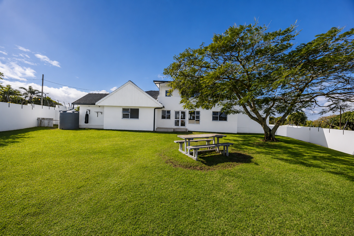 Spacious rear garden featuring a well-maintained lawn, mature tree, and secure perimeter walling with a water tank.