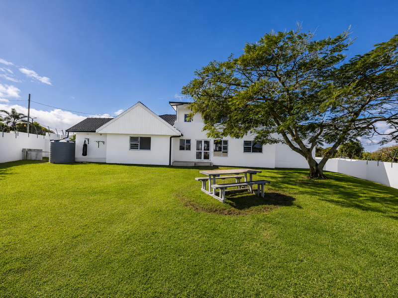 Spacious rear garden featuring a well-maintained lawn, mature tree, and secure perimeter walling with a water tank.
