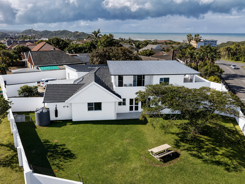 Aerial view of a modern residential property featuring a white exterior, metal roofing, a spacious garden, and a secure perimeter wall.