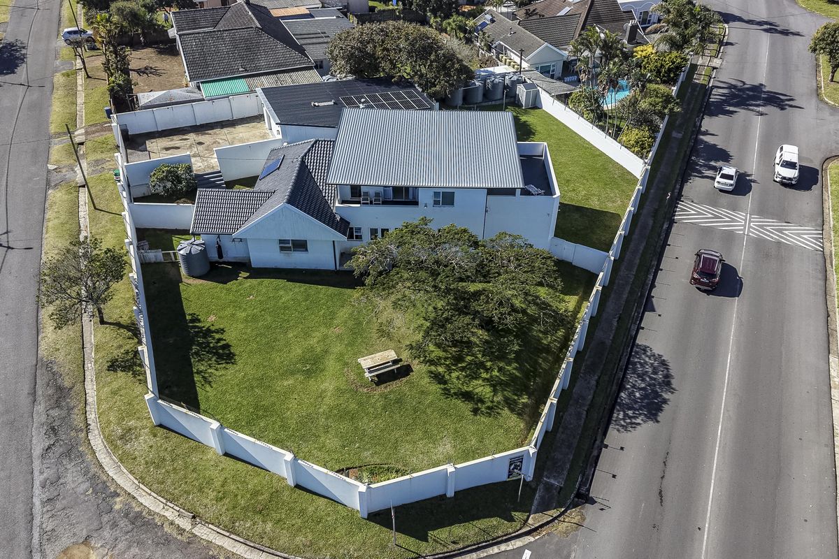 Aerial view of a corner property featuring a large garden, perimeter wall, and solar panels installed on the roof.