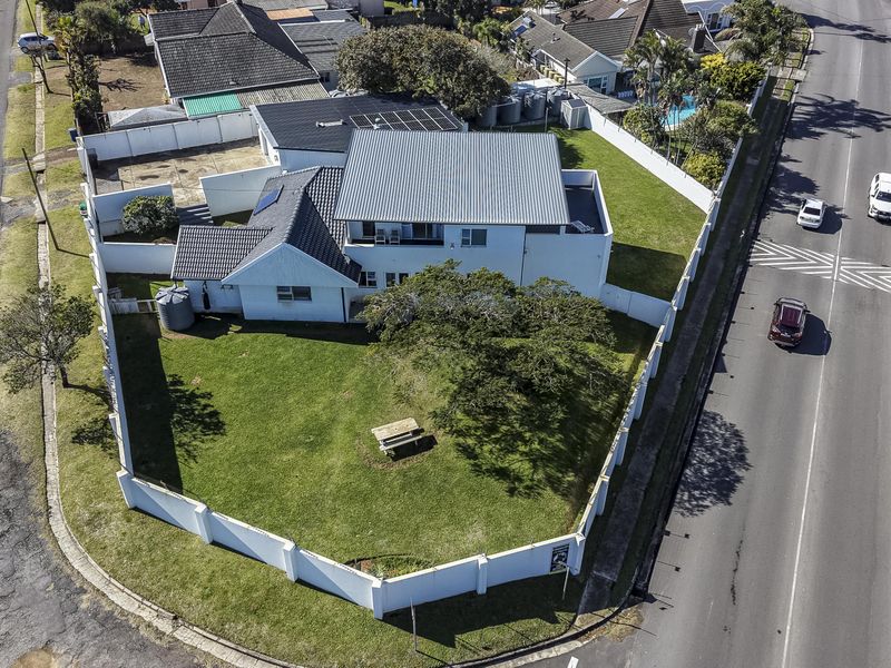 Aerial view of a corner property featuring a large garden, perimeter wall, and solar panels installed on the roof.
