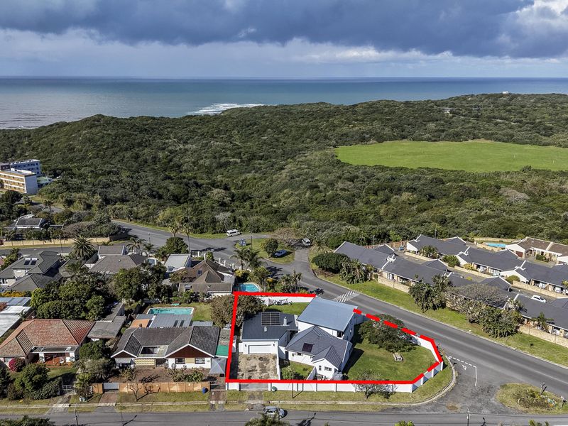 Aerial view of a residential property featuring a metal roof with solar panels, a paved driveway, and a perimeter boundary wall in a coastal setting.