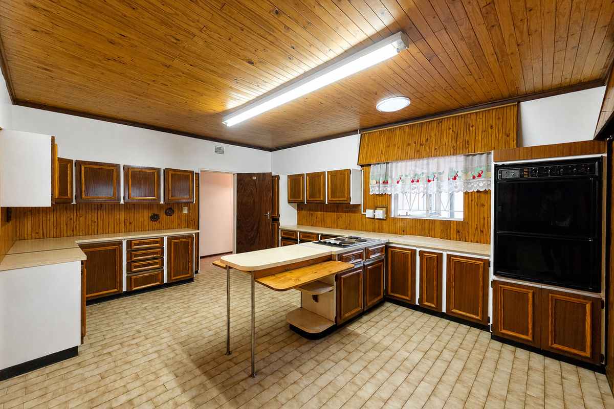 Spacious kitchen featuring extensive wooden cabinetry, built-in oven, electric hob, and classic wood-paneled ceilings, offering a functional layout ready for modern updates.