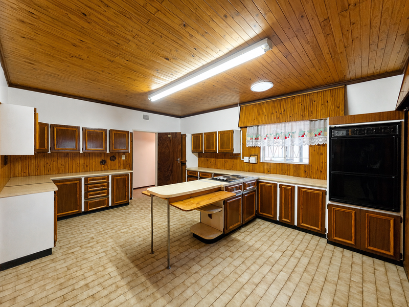 Spacious kitchen featuring extensive wooden cabinetry, built-in oven, electric hob, and classic wood-paneled ceilings, offering a functional layout ready for modern updates.