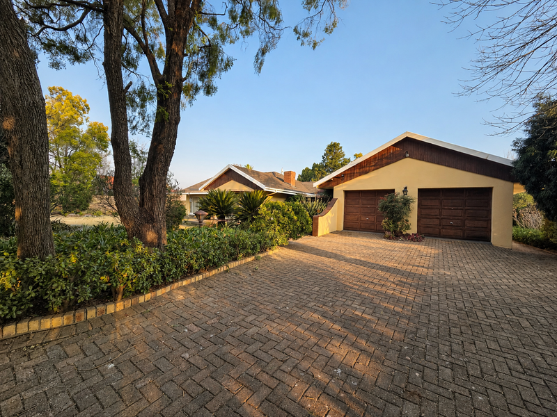 Front view of a residential property featuring a paved driveway, double garage, and established garden landscaping.