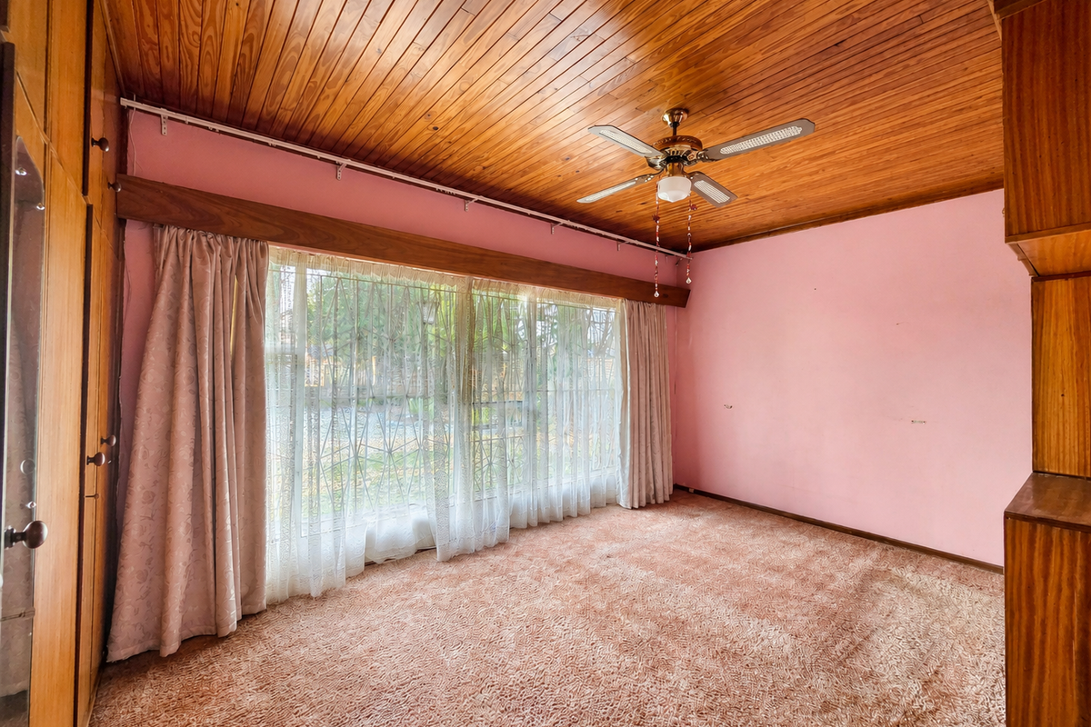 Spacious bedroom featuring a timber-clad ceiling, built-in cupboards, and large windows with security bars, offering a blank canvas for renovation.