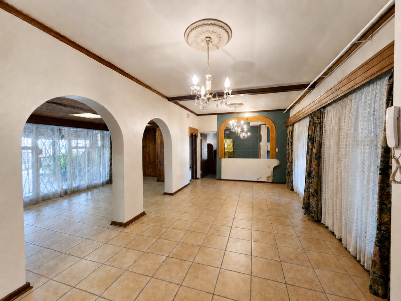 Spacious living area featuring ceramic floor tiles, arched architectural details, and decorative ceiling fixtures, offering a blank canvas for renovation.