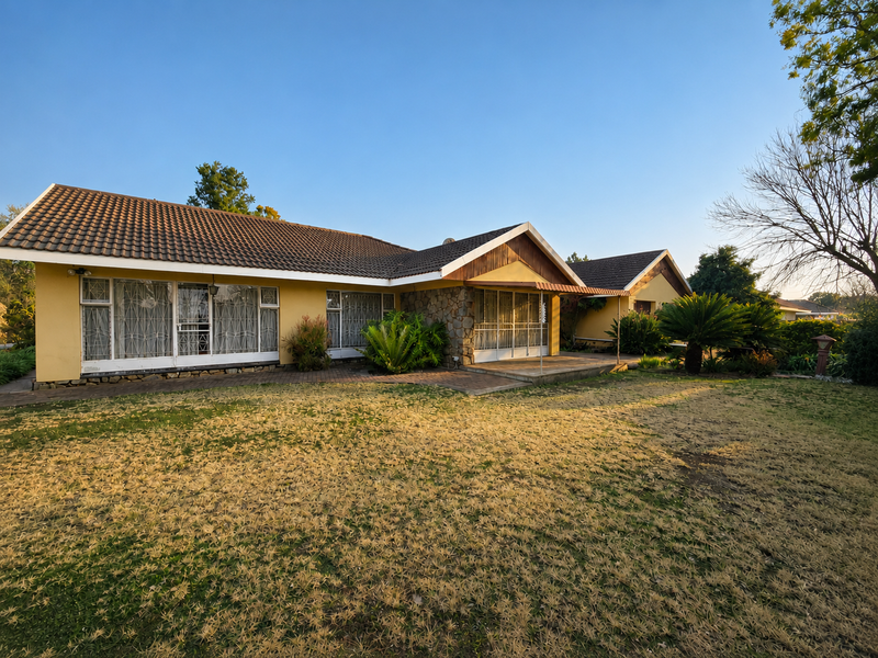 Rear view of a single-story house featuring a tiled roof, stone facade accents, and a paved patio area overlooking a large garden.