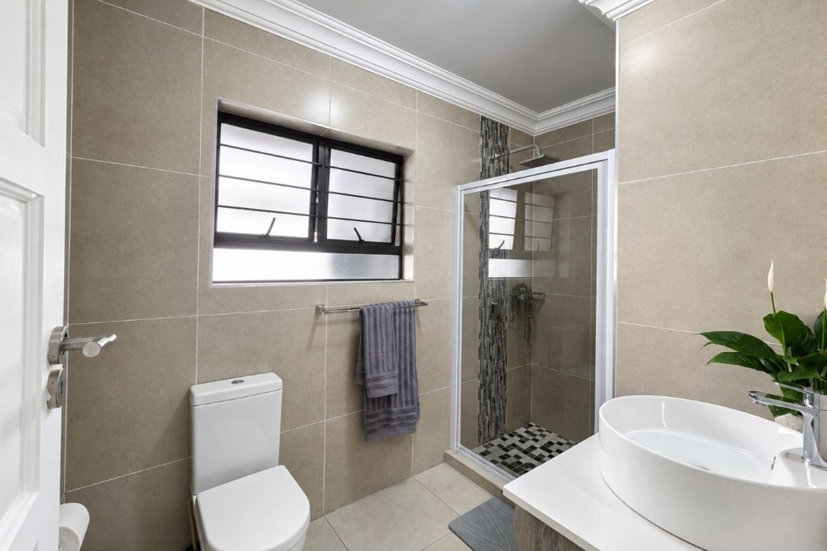 Modern bathroom featuring a glass-enclosed shower, vessel sink vanity, neutral wall tiling, and decorative ceiling cornice.