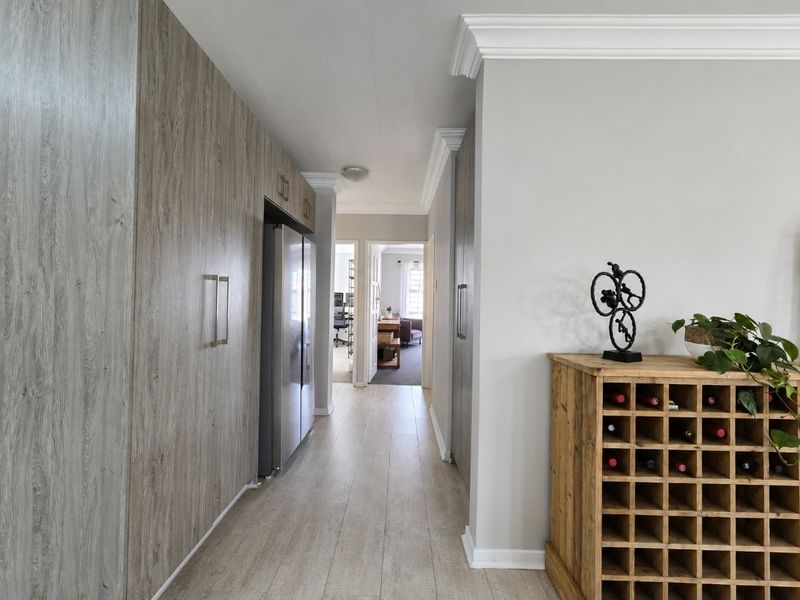 A well-maintained hallway featuring modern wood-look cabinetry, crown molding, and light-toned laminate flooring, leading through to an adjacent living space.