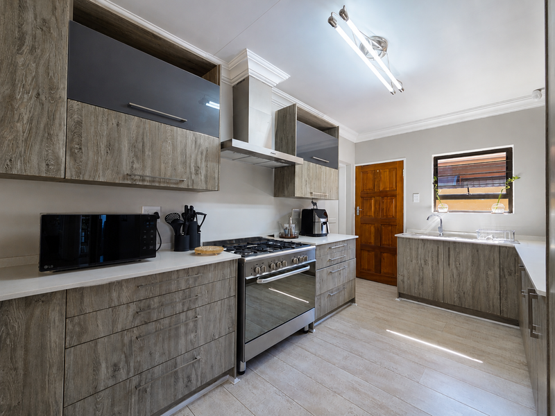 Modern kitchen featuring wood-grain cabinetry, quartz countertops, a stainless steel gas stove with extractor fan, and tiled flooring.