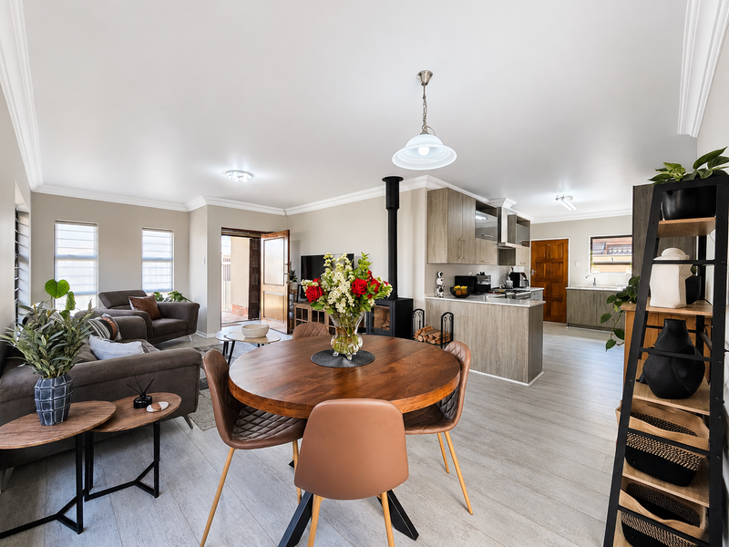 Spacious open-plan living and dining area featuring a wood-burning fireplace, modern kitchen cabinetry, and neutral tiled flooring throughout.