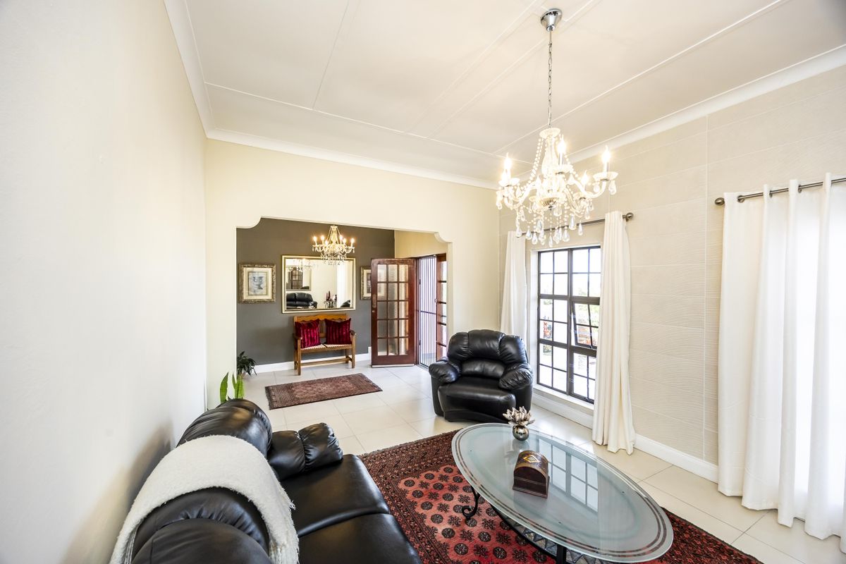 Spacious living room featuring tiled flooring, a decorative crystal chandelier, coved ceilings, and a timber-framed glass door leading to an adjacent area.