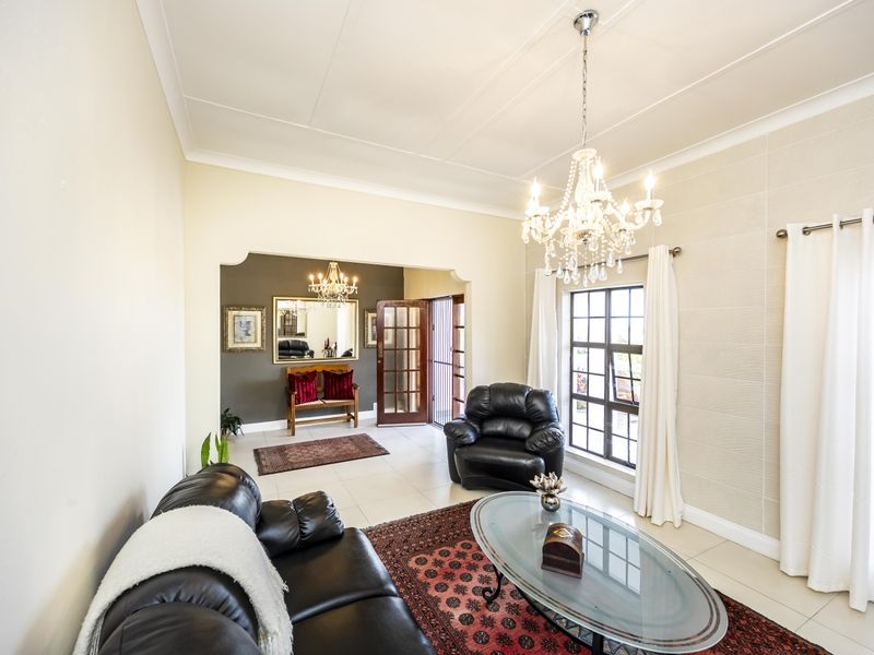 Spacious living room featuring tiled flooring, a decorative crystal chandelier, coved ceilings, and a timber-framed glass door leading to an adjacent area.