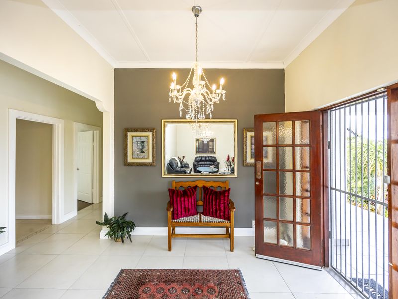 A bright and welcoming entrance hall featuring tiled flooring, a decorative crystal chandelier, and a timber-framed glass front door with security gate.