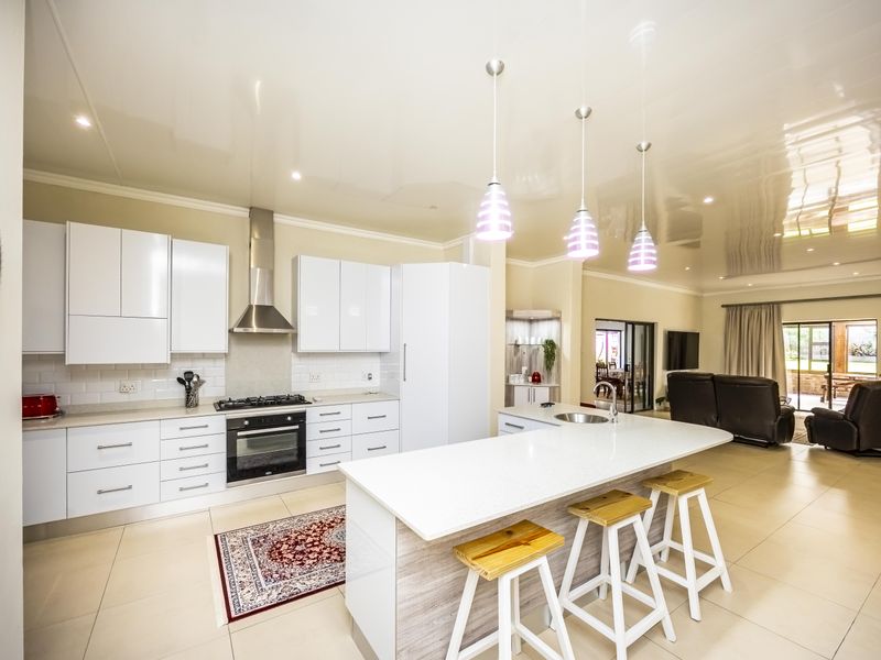 Modern open-plan kitchen featuring glossy white cabinetry, a stone island with breakfast bar, and integrated appliances, flowing seamlessly into the adjacent living area.