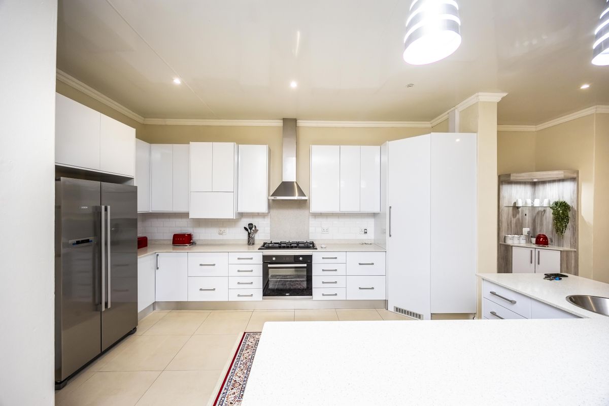 Modern kitchen featuring white high-gloss cabinetry, stone countertops, a central island, and integrated stainless steel appliances with a subway tile backsplash.